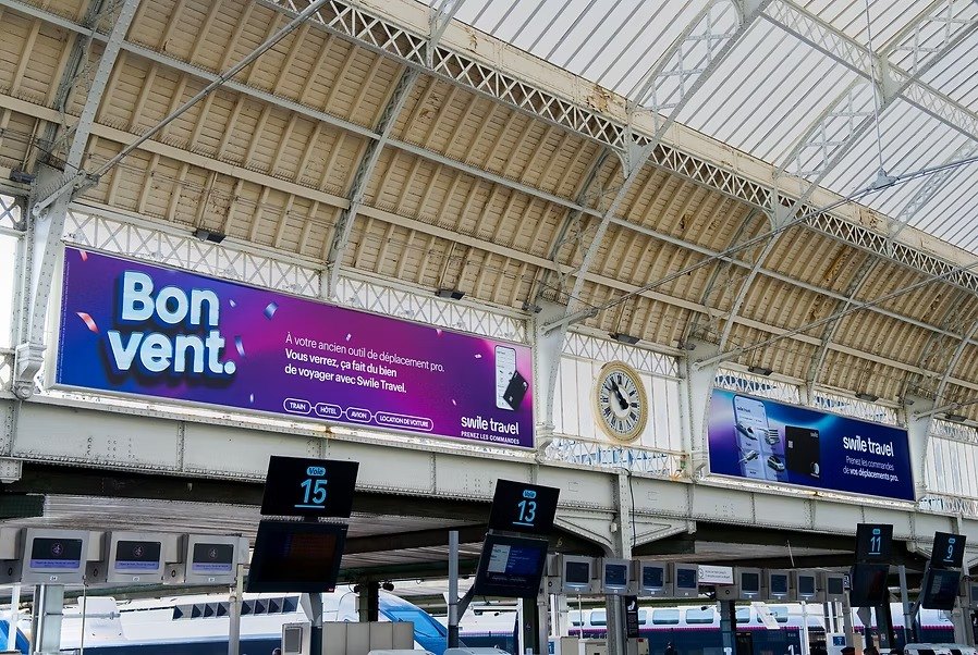 Affiche « Bon vent. » au-dessus des quais d'une gare.
